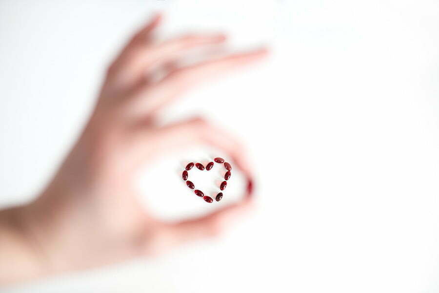 Bilde av Zooca kapsler formet som et hjerte i bakgrunnen, hvor en hånd er i forgrunne og omfavner hjertet